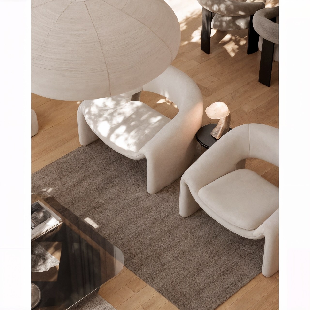 Overhead view of curved lounge chairs, a rug and sculptural pendant lights in a warm living room.
