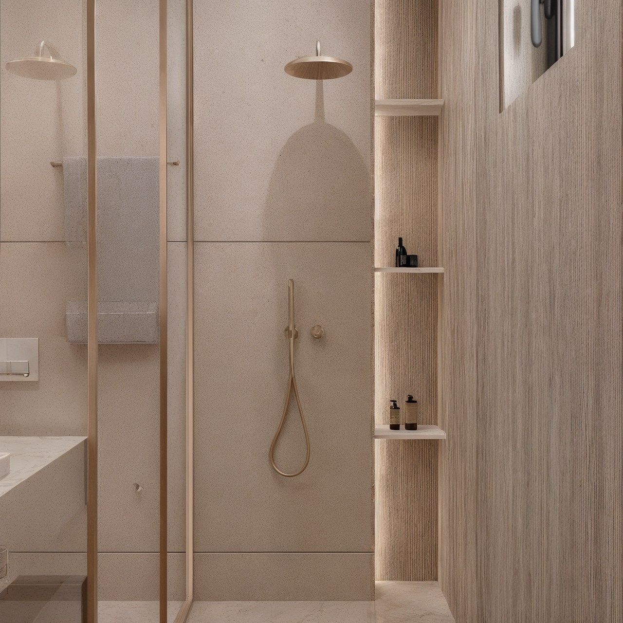 Walk-in shower with pale stone surfaces, recessed shelf and warm brass fittings.