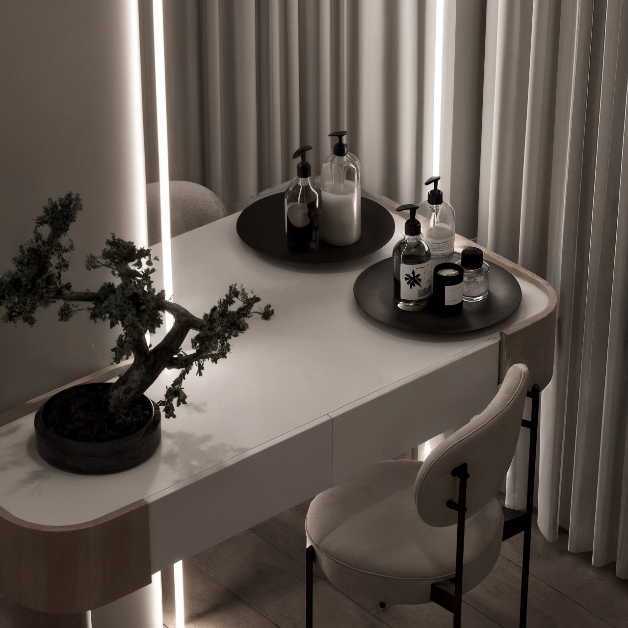 Compact vanity desk with curved chair, bonsai and grooming accessories beside floor-to-ceiling curtains.